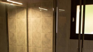 A modern bathroom with a glass-enclosed shower, a sink with a mirror, and tiled walls. - Hôtel restaurant Marinet (Valserhône)