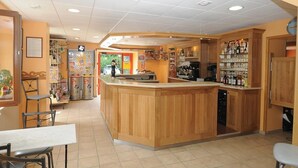 A restaurant with a wooden bar area, seating, and a counter with various items. - Hôtel restaurant Marinet (Valserhône)