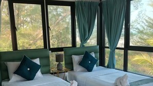 A hotel room with two beds, each with a green headboard, white bedding, and blue pillows. There are towels folded on the beds, and the room has large windows with curtains. - Veerada Boutique Home (Chaiya)