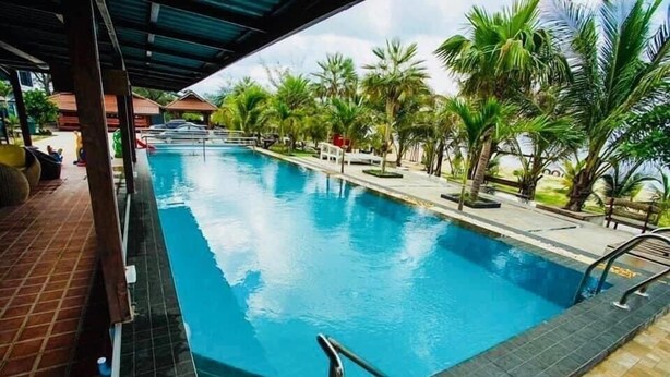 A swimming pool with a tiled edge, surrounded by palm trees and a covered area with a tiled floor. - Veerada Boutique Home (Chaiya)