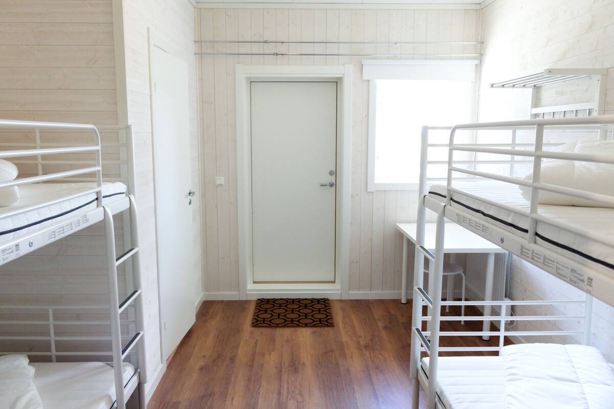 Una habitación con literas, una puerta, una ventana y suelo de madera.