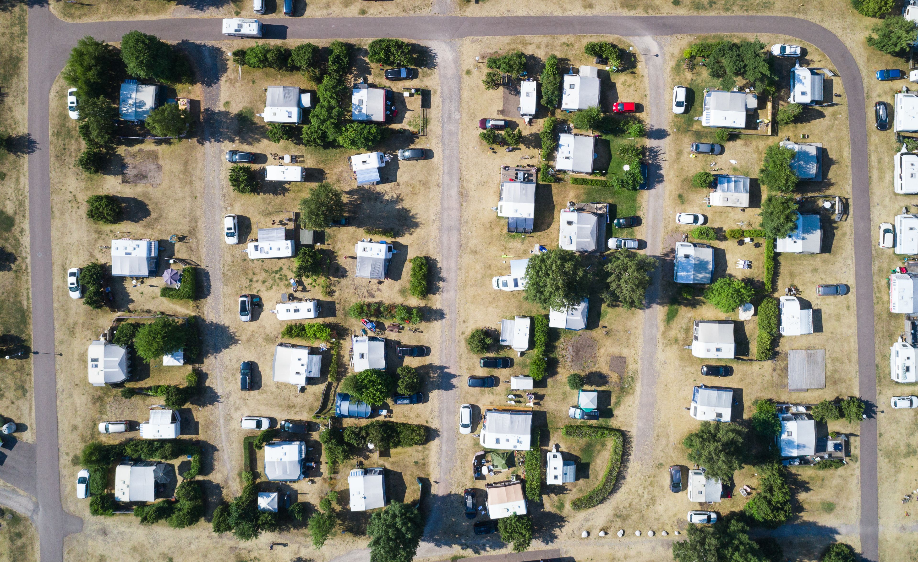 An aerial view of a campground with RVs and trailers arranged in rows, surrounded by trees and grassy areas.