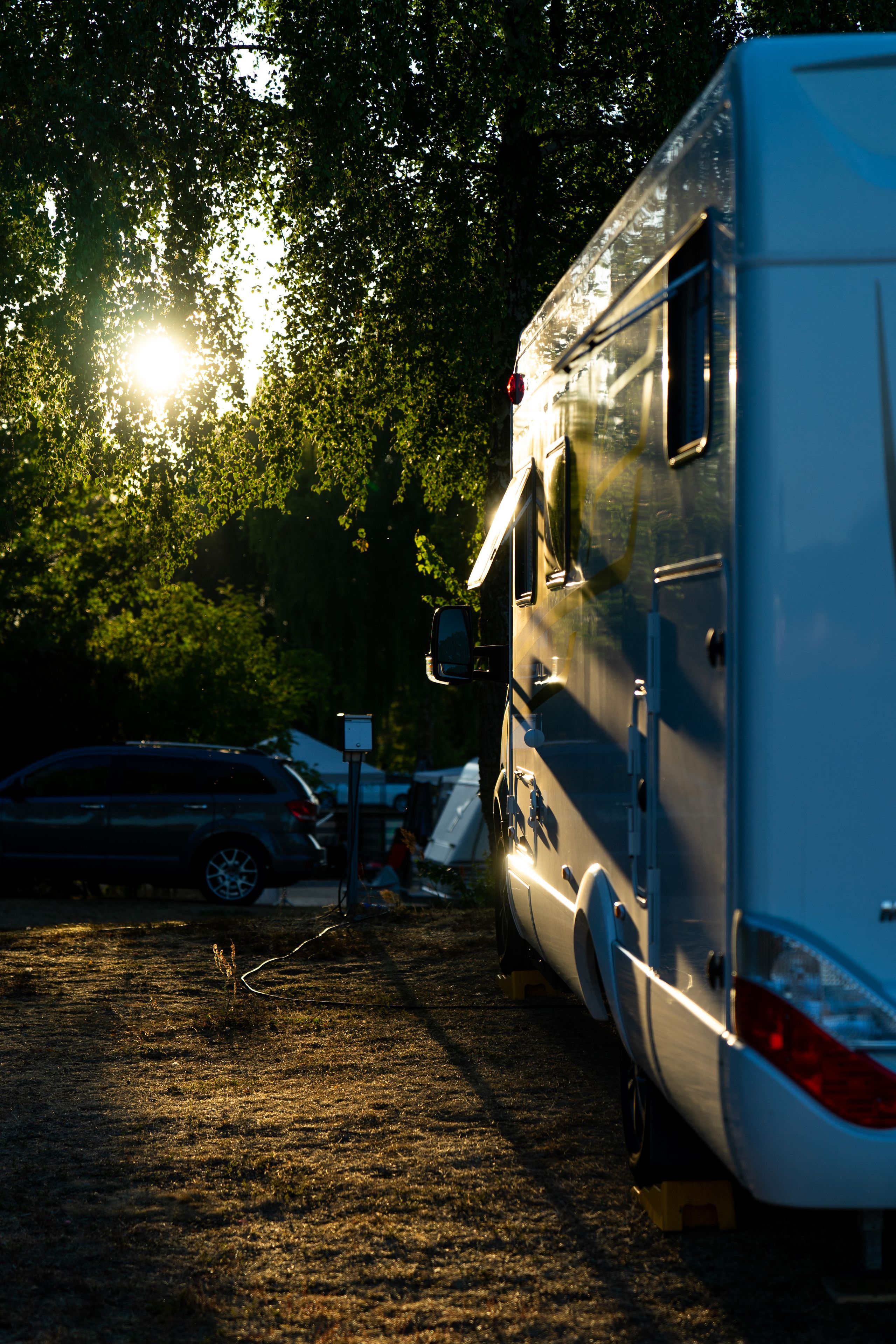 A campsite with a trailer and a car parked on a dirt ground.