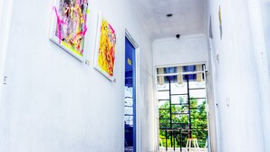 Un pasillo con una puerta azul, una ventana con vistas a zonas verdes y dos obras de arte en la pared.
