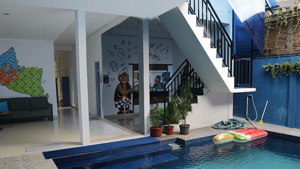 Una piscina interior con borde de azulejos azules, plantas en macetas y un juguete flotando.