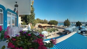 A balcony with a view of a marina, outdoor seating, and a white building with blue trim. - Denizkizi Motel (Ayvacik)