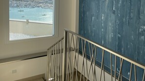 Ein Zimmer mit großem Fenster mit Blick auf einen Hafen, einer Treppe mit Metallgeländer und einem blauen abstrakten Gemälde an der Wand.