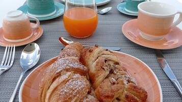 A table with croissants and orange juice, set against a scenic view of a marina.