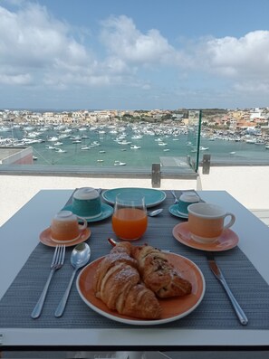 A table set with croissants, orange juice, and coffee, overlooking a marina with boats and buildings. - Giro di Boa (Lampedusa)