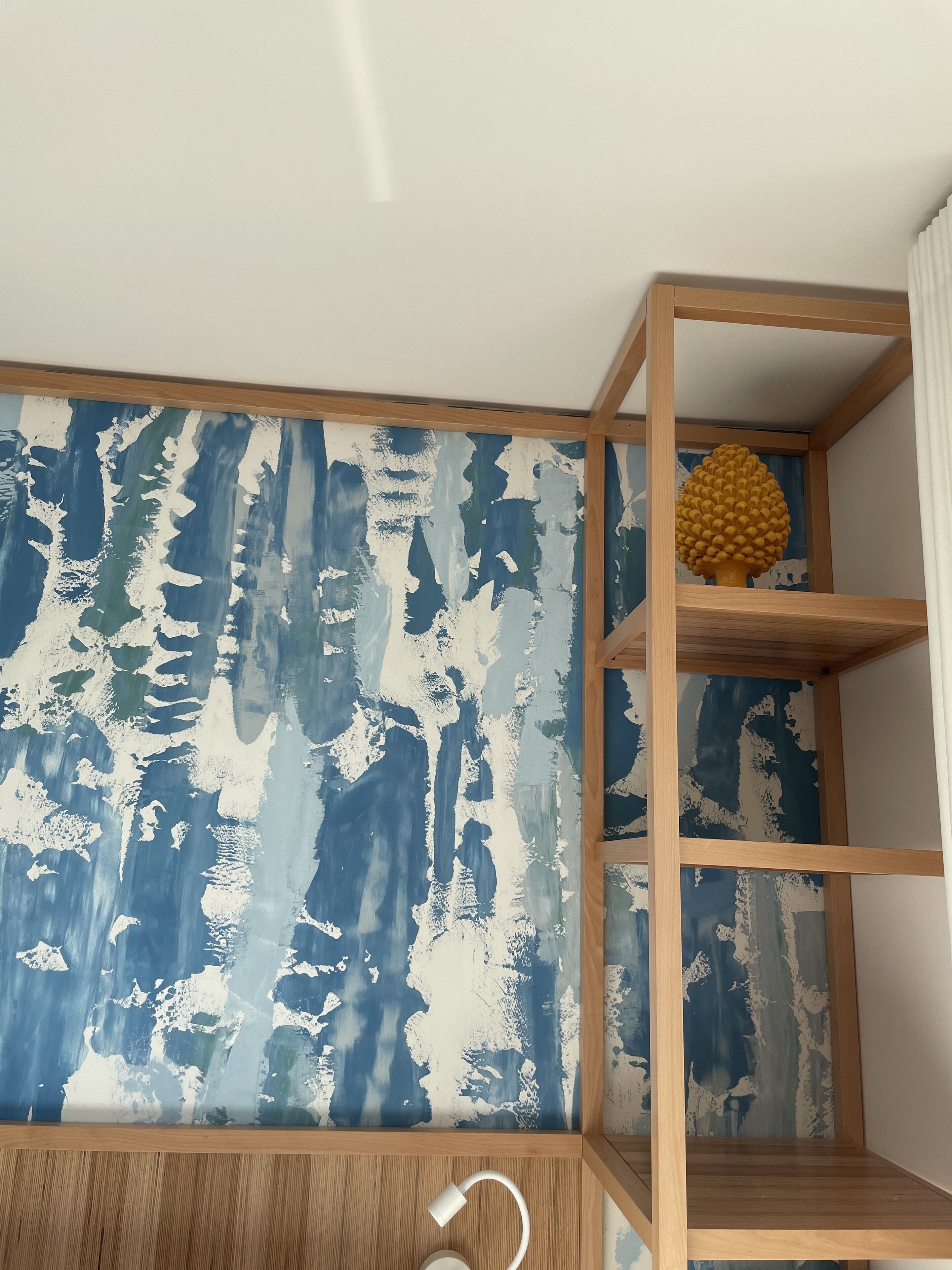 A room with a wooden shelf unit against a wall with a blue and white abstract pattern.