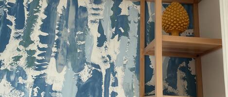 A room with a wooden shelf unit against a wall with a blue and white abstract pattern.