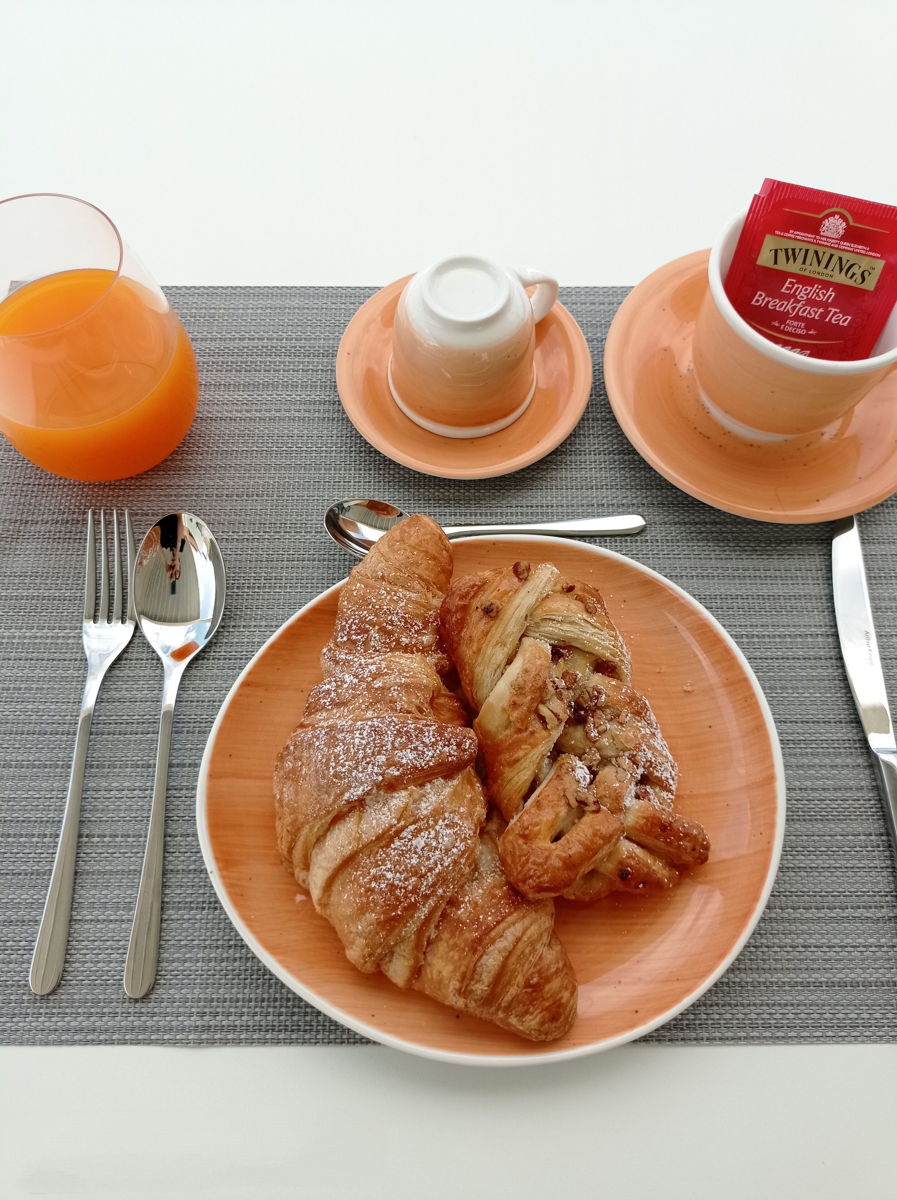 A breakfast setting with croissants, a cup of English breakfast tea, and a glass of orange juice.