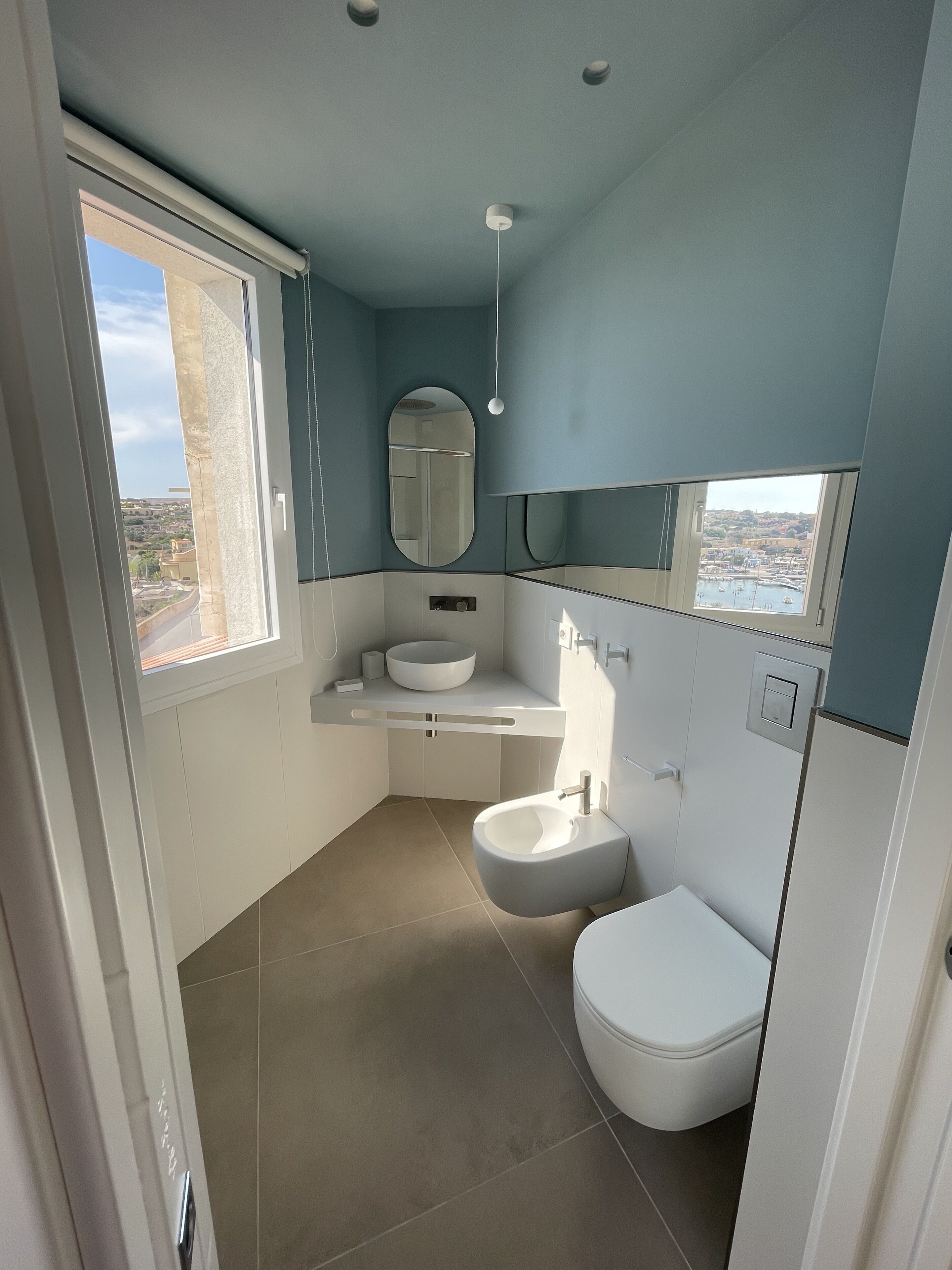 A modern bathroom with a large window, a sink, a toilet, and a mirror.