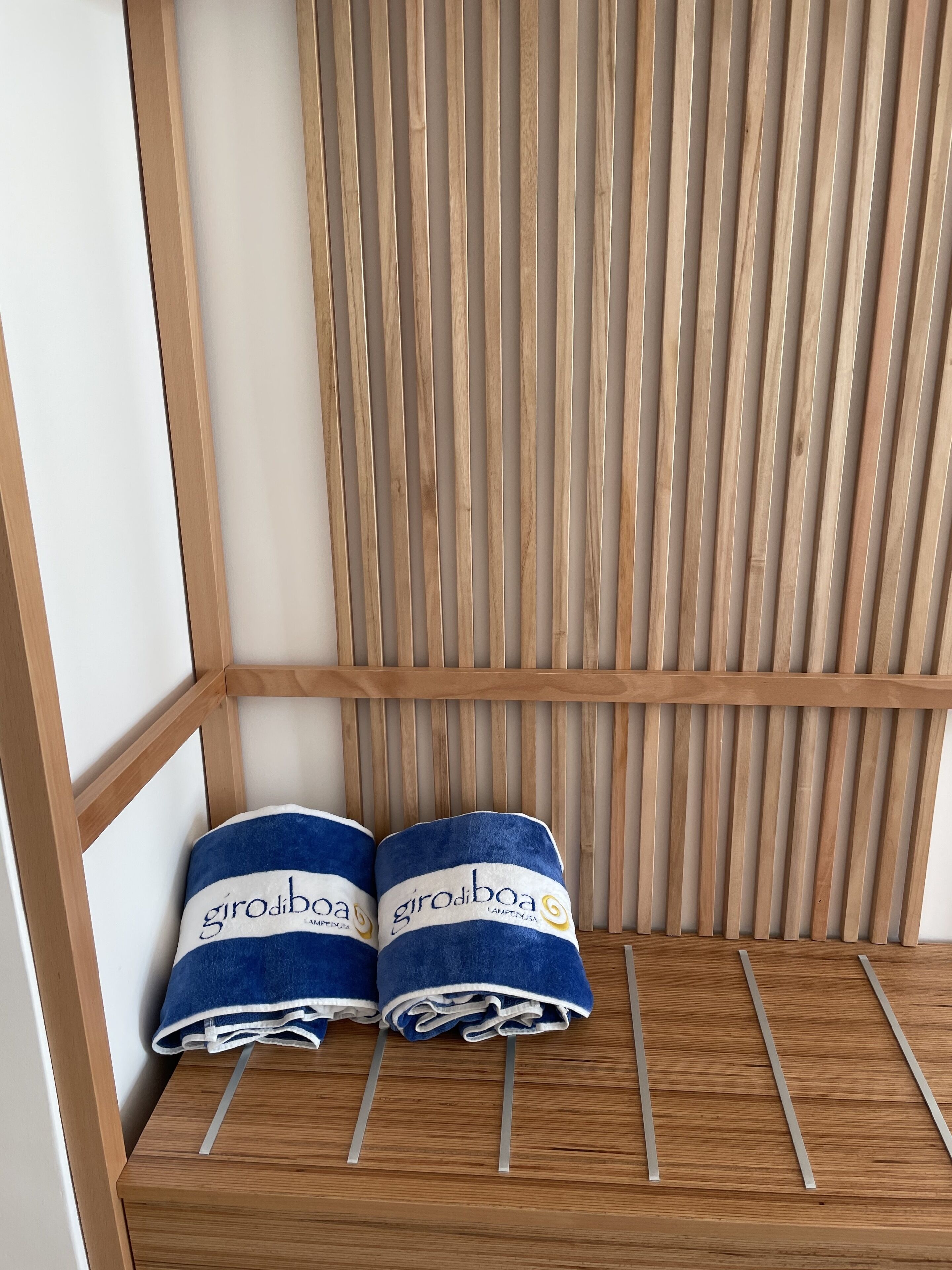 Dos toallas con la marca "girodiboa" sobre un estante de madera frente a una pared con listones de madera.