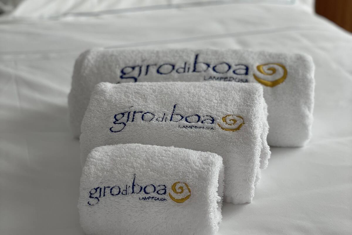 A neatly made bed with white linens and three folded towels with 'groboa' branding on a hotel room.