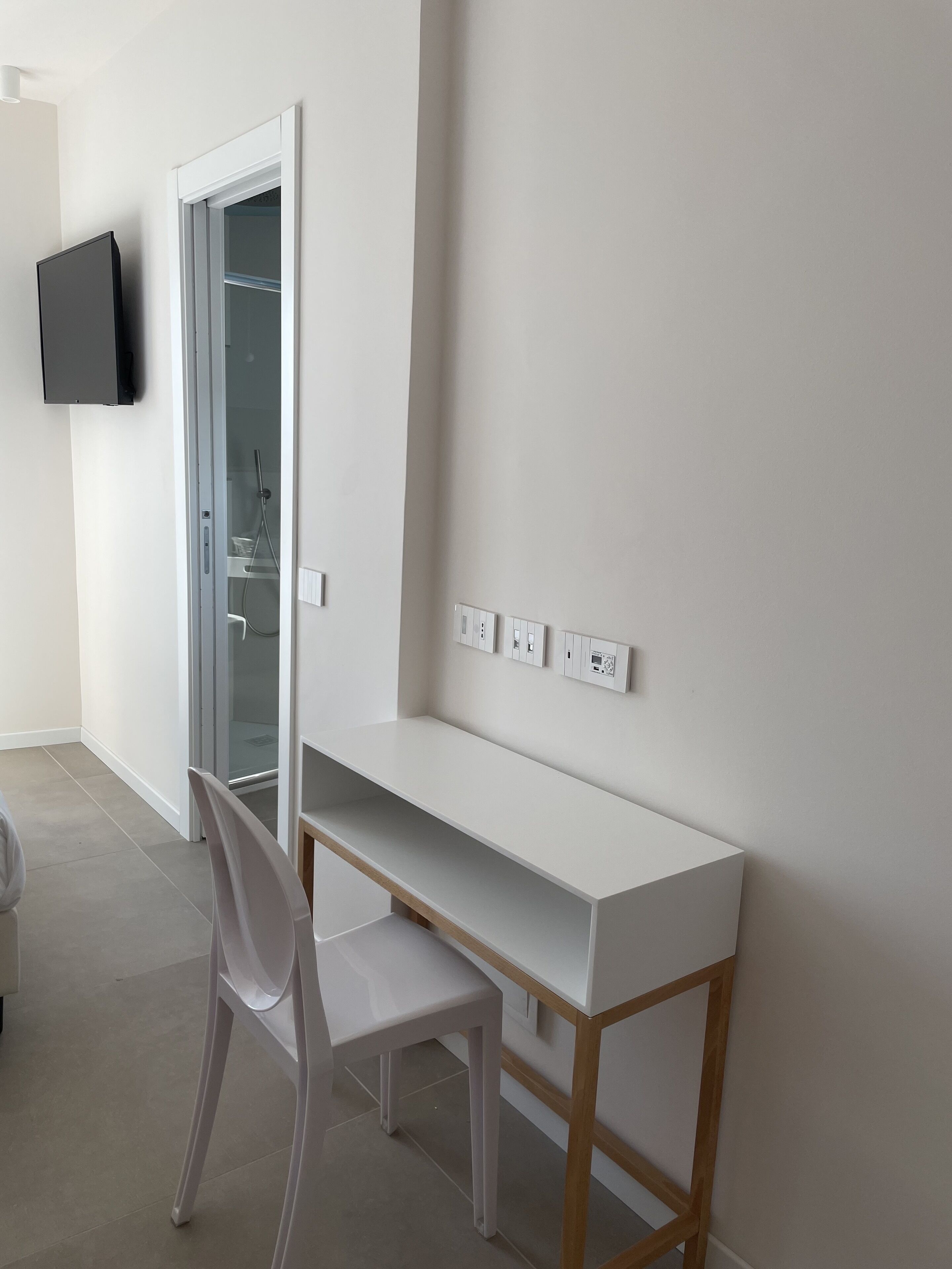 Une pièce moderne et minimaliste, avec un bureau blanc, une chaise et un téléviseur à écran plat fixé au mur.