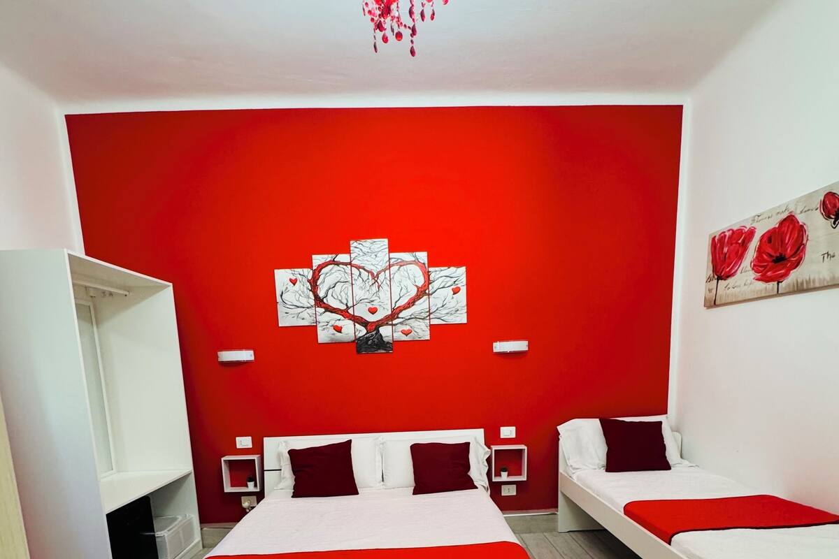 Ein Schlafzimmer mit zwei Betten, einer roten Akzentwand, einem Kronleuchter und einem herzförmigen Kunstwerk.