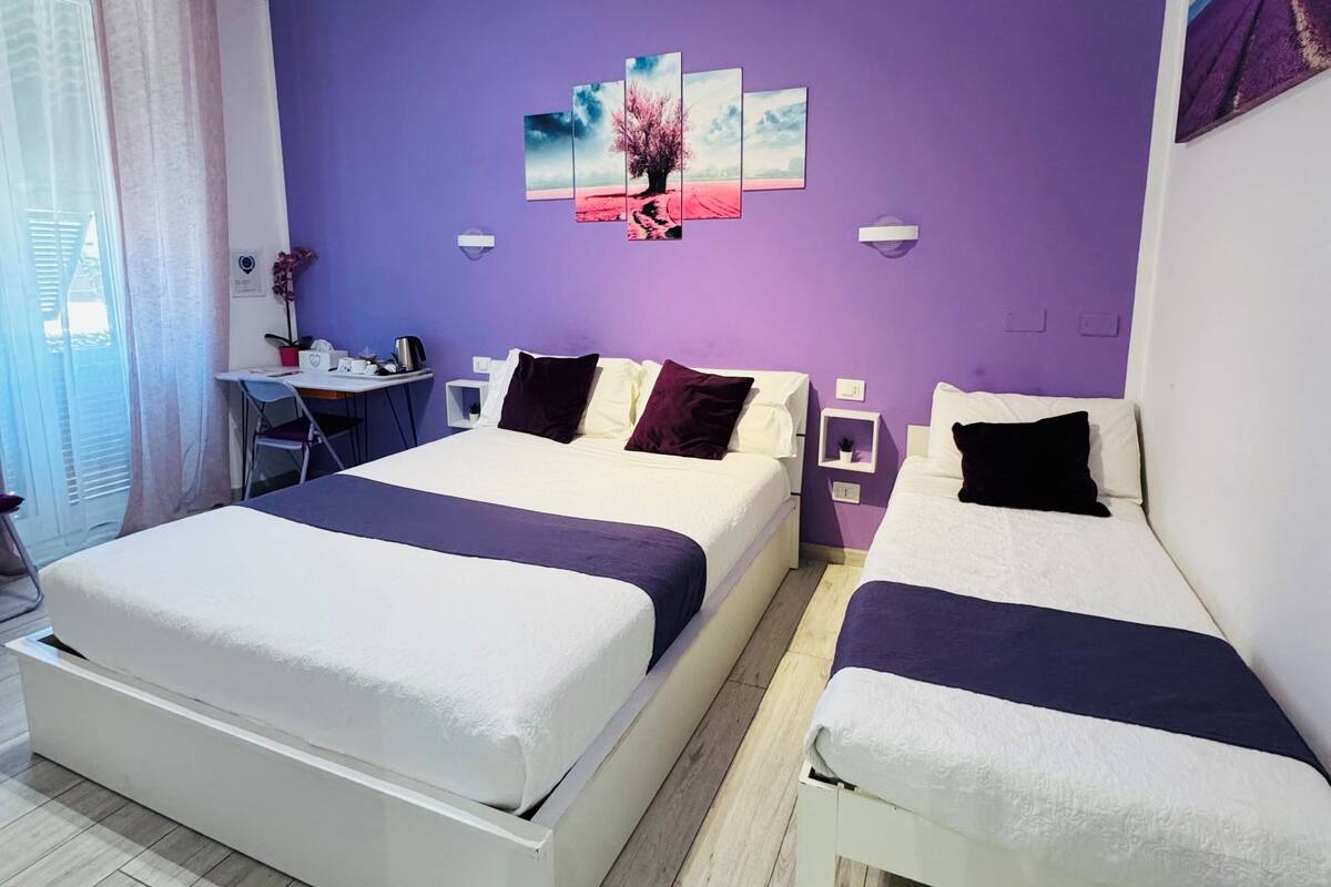 Ein modernes Hotelzimmer mit zwei Betten, einem Schreibtisch und einer violetten Wand.