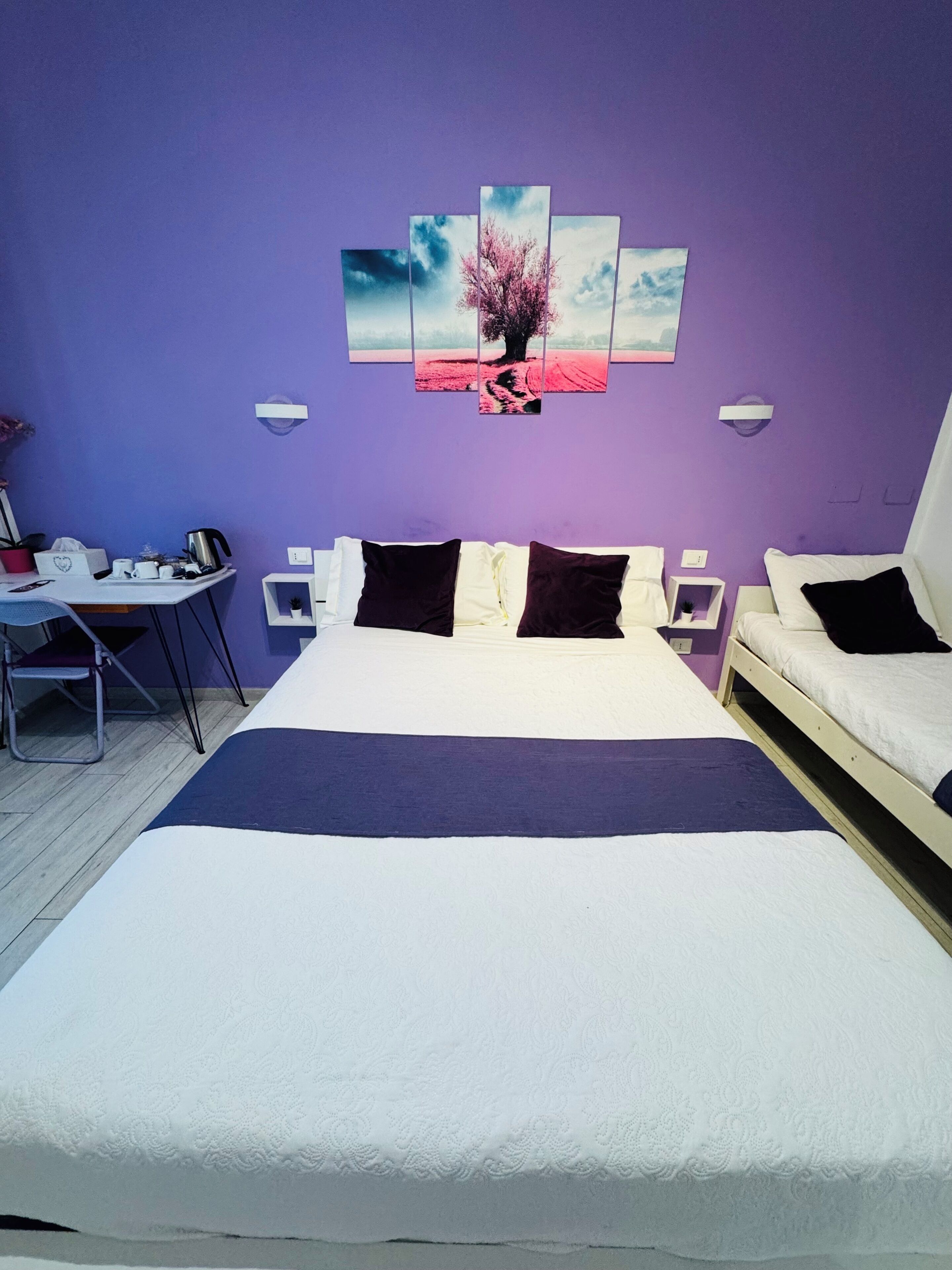 A bedroom with a large bed, a desk with a chair, and a wall-mounted artwork.