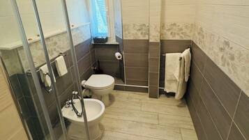 Een badkamer met een douchecabine van glas, een toilet en een bidet.