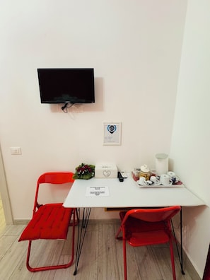 A small room with a white table, two red chairs, a television mounted on the wall, and a framed certificate on the wall.