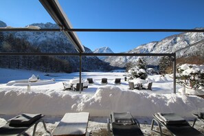 A snow-covered outdoor seating area with lounge chairs and tables, overlooking a snowy landscape and mountains. - Hotel Seeblick (Bad Reichenhall)