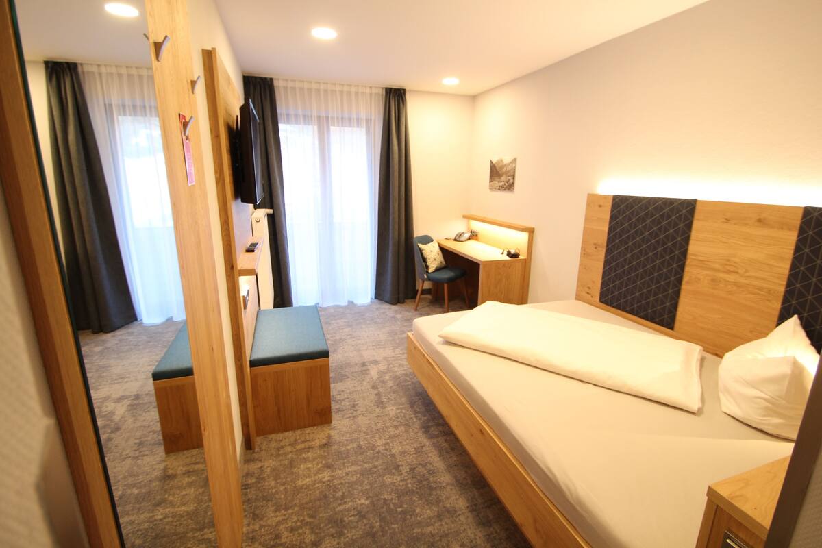 Quarto de hotel com cama, escrivaninha, cadeira e televisão.