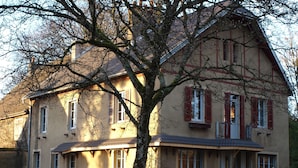A two-story house with a sloped roof, multiple windows with shutters, and a front porch with outdoor seating. - Chambre d'hôte Calme et Volupté (Maxilly-sur-Saône)