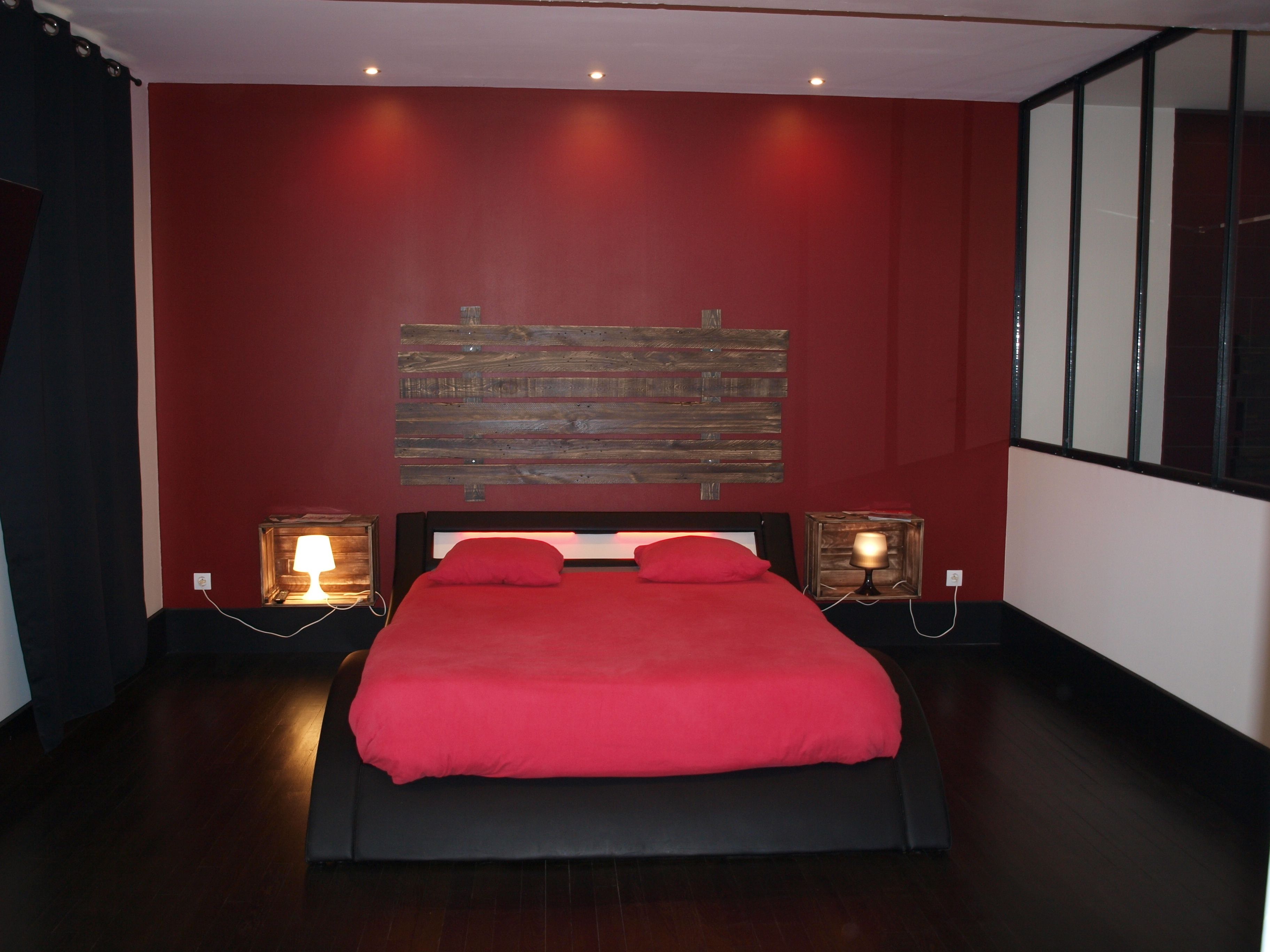 A bedroom with a large bed, red walls, and a wooden headboard. There are two bedside lamps and a window on the right.
