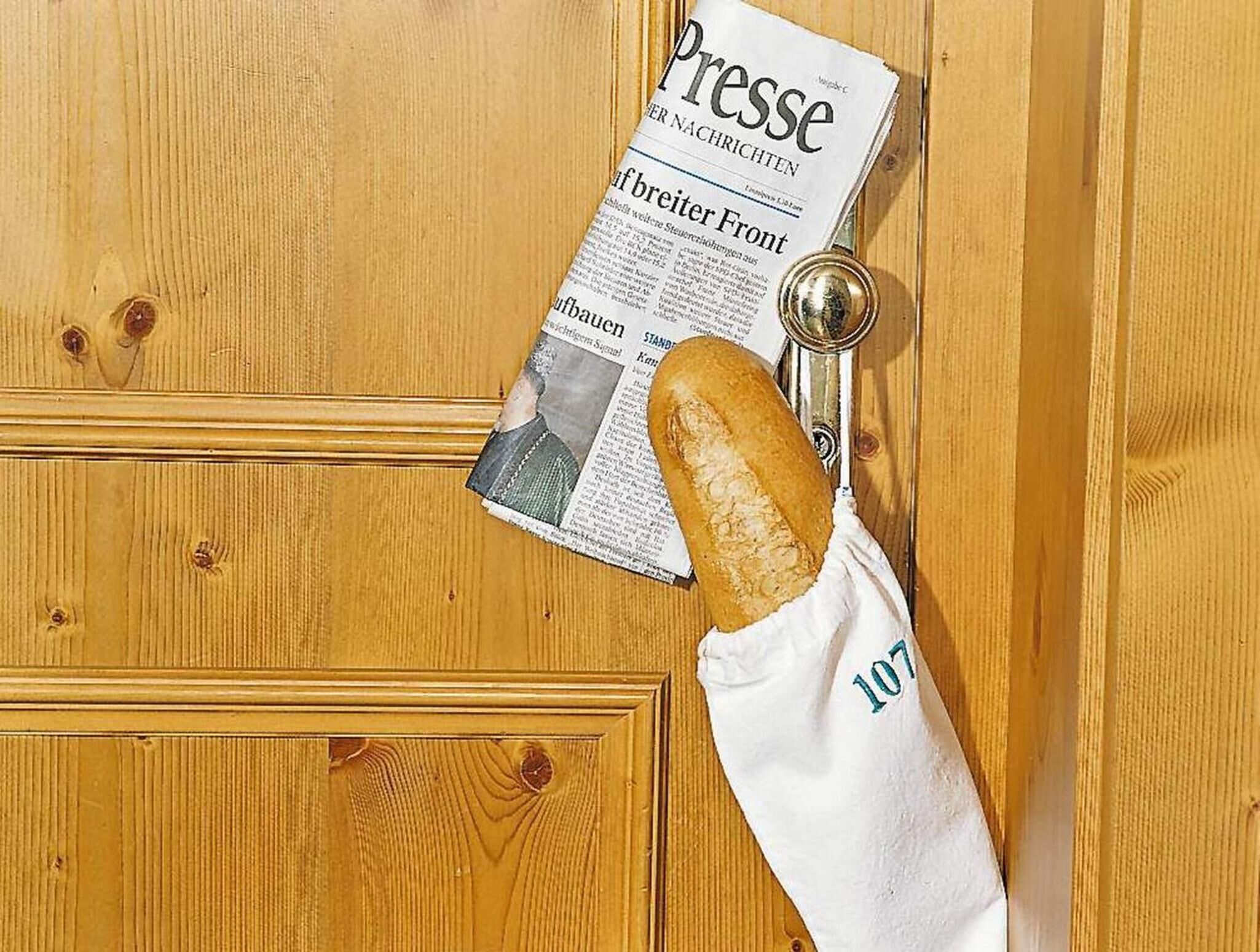 A wooden door with a newspaper titled 'Presse' and a baguette in a white cloth bag.
