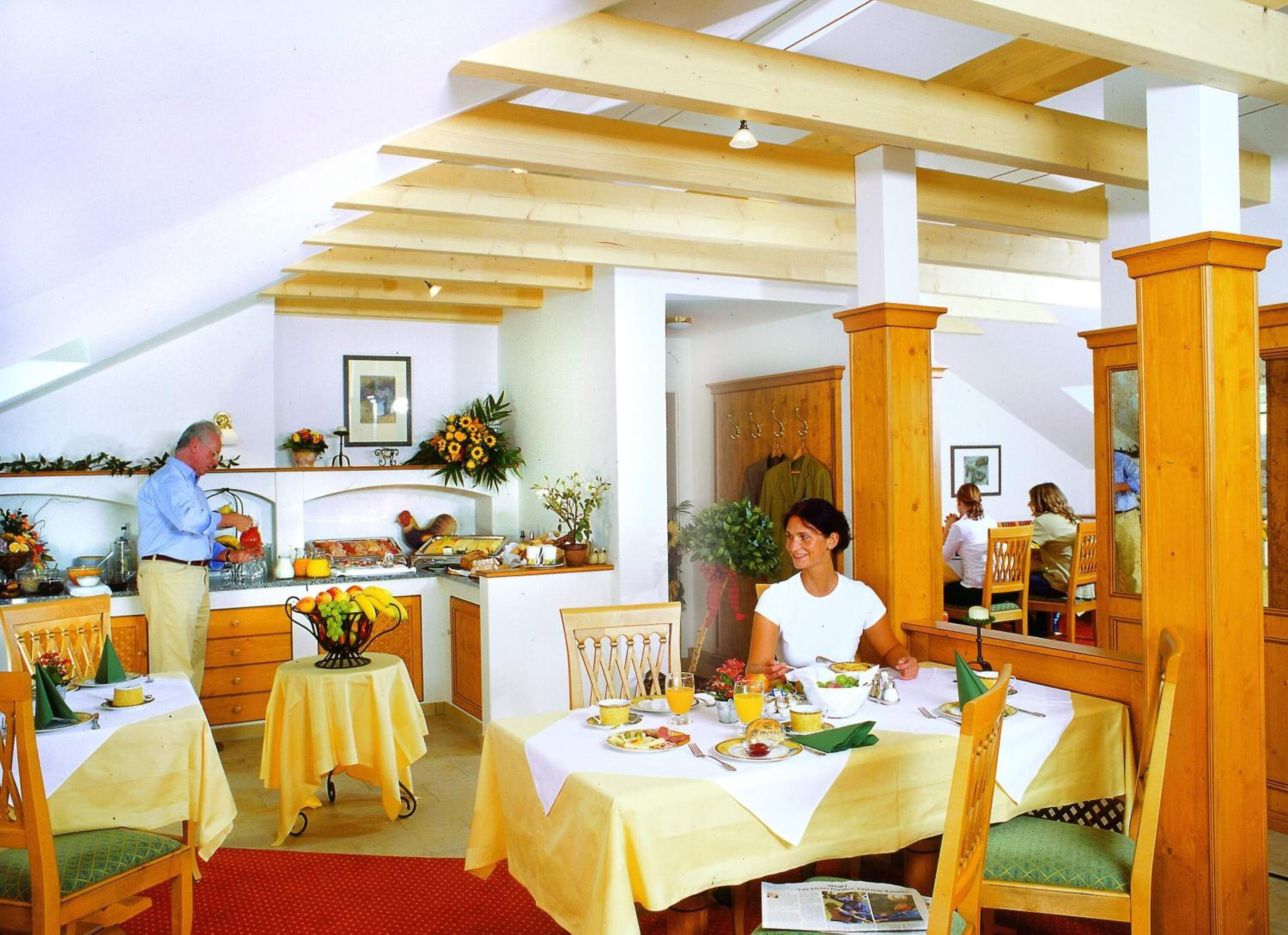 Uma área de refeições com mesas e cadeiras de madeira, uma cozinha com balcão e uma mesa de jantar posta para uma refeição.