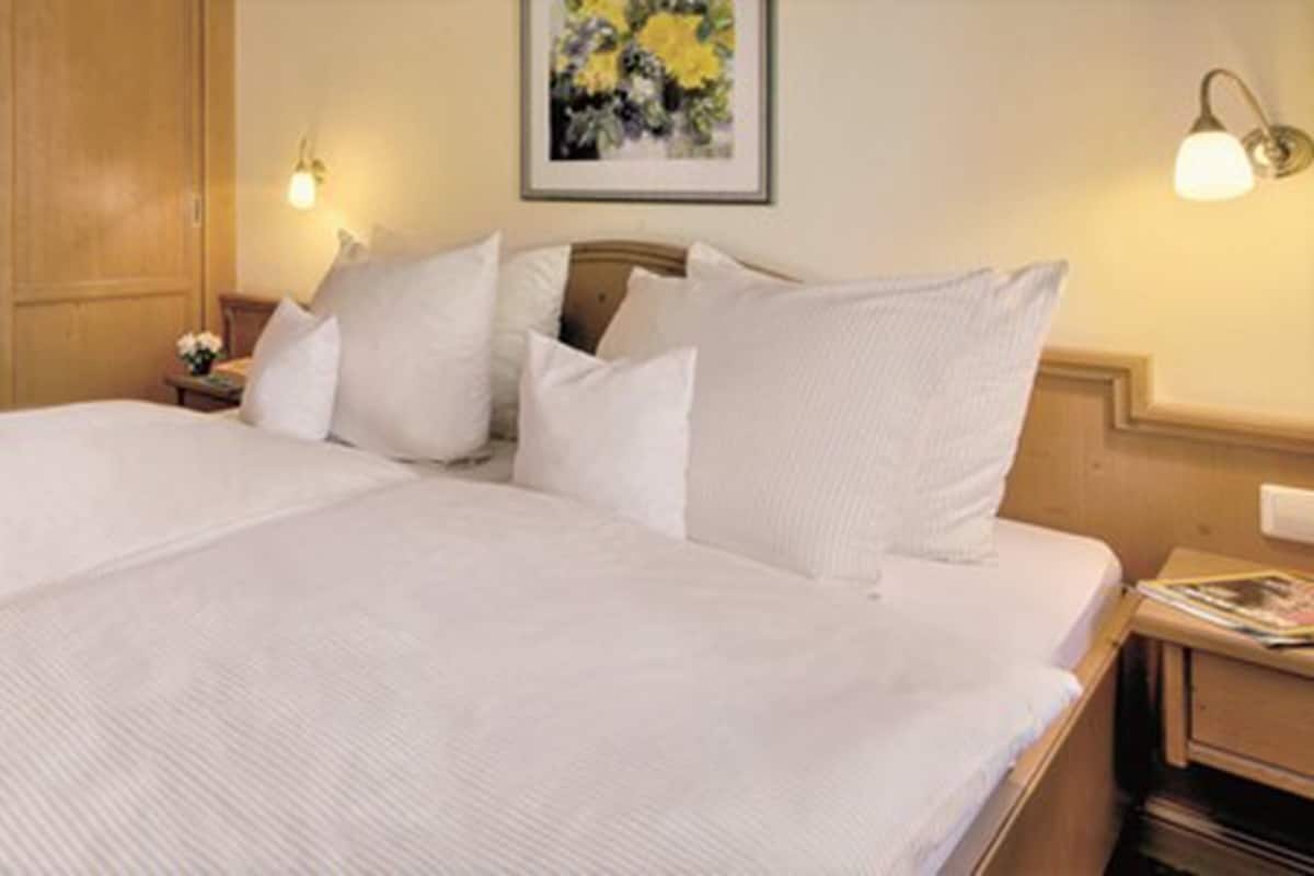 Una cama bien hecha con sábanas y almohadas blancas, un cabecero de madera y dos lámparas de noche.