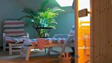 Relax in a cozy room with a sloped ceiling, featuring a window and two lounge chairs for socializing or unwinding.