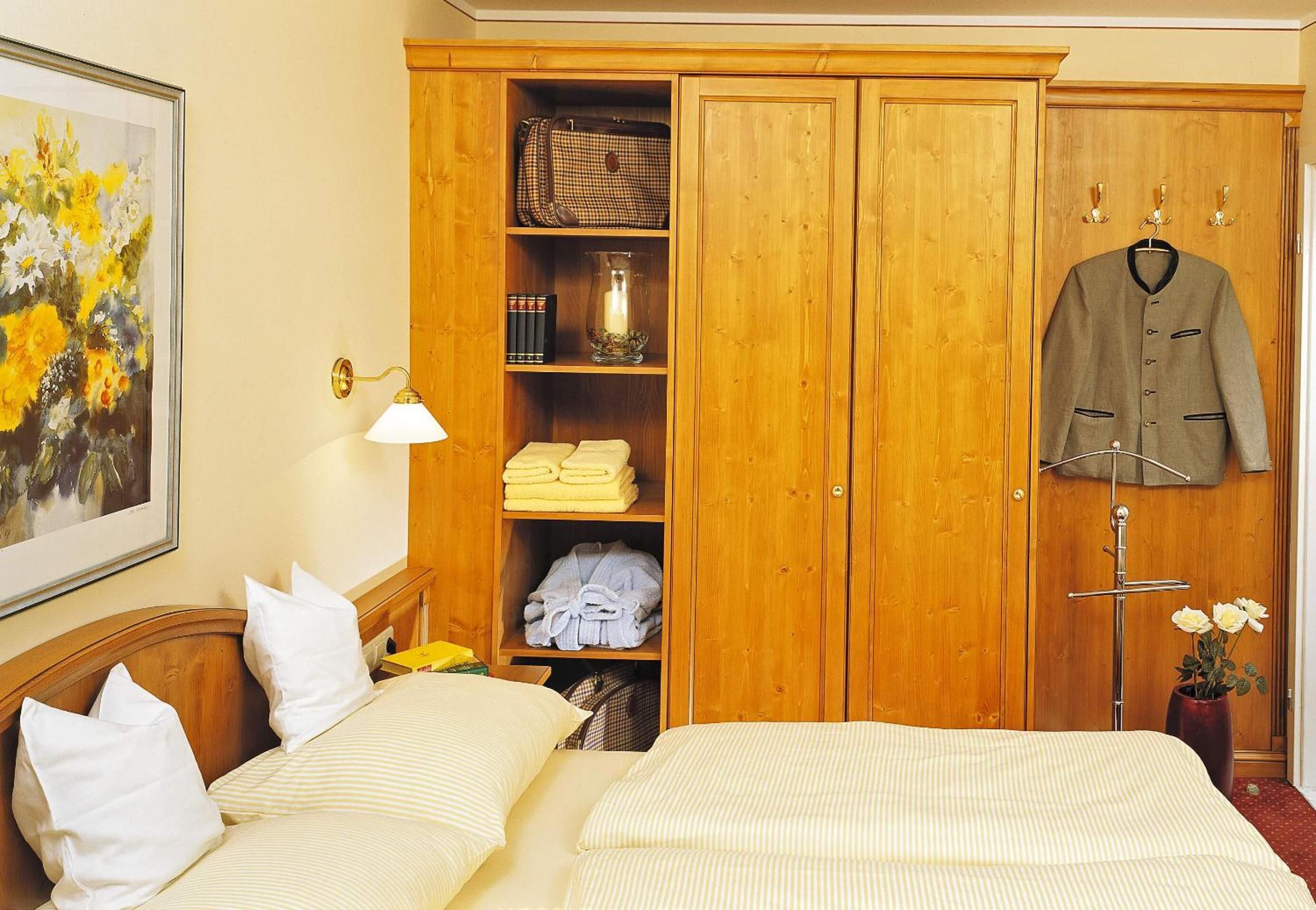 Ein Hotelzimmer mit Bett, einer Schrank mit Regalen, einem Kleiderhaken und einem Bild an der Wand.