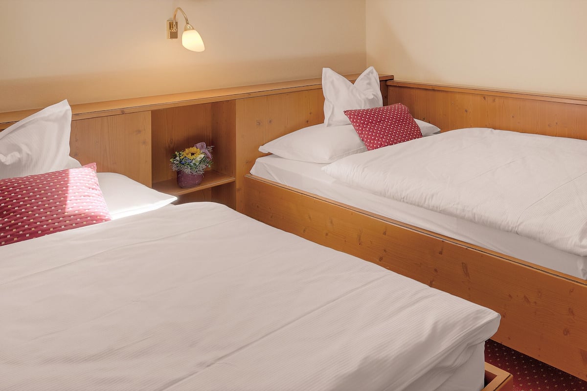 Dos camas individuales con cabeceros de madera, ropa de cama blanca y una pequeña estantería con un jarrón de flores.