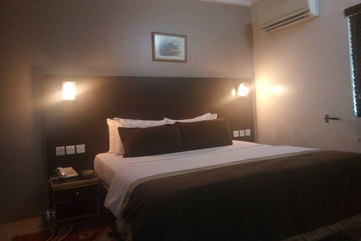 A hotel room with a bed, bedside table, and a wall-mounted air conditioner.
