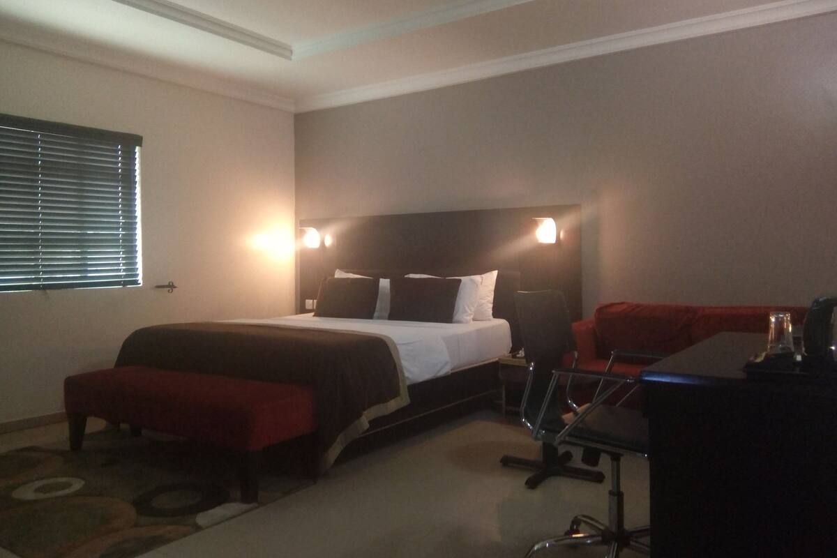 A hotel room with a bed, a desk, a chair, and a window with blinds.