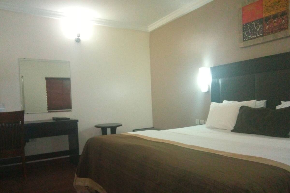 A hotel room with a bed, a small table, a chair, a desk, and a mirror.