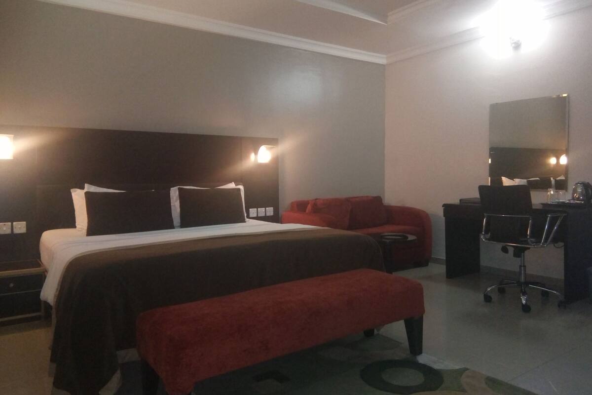 A hotel room with a bed, a red sofa, a desk with a chair, and a mirror.