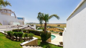 A modern building with a pool, palm trees, and a view of the countryside.