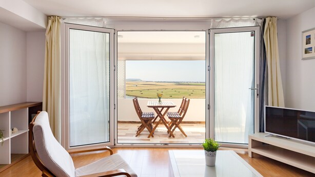 A room with a sofa, a TV, a glass table, and a balcony with a table and chairs.