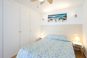 Una camera da letto con un letto, due comodini con lampade, una ventola a soffitto, un quadro appeso al muro e un armadio.