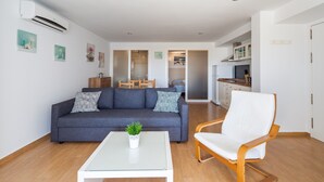 A modern living room with a sofa, a coffee table, and a chair. There is a kitchen area in the background.