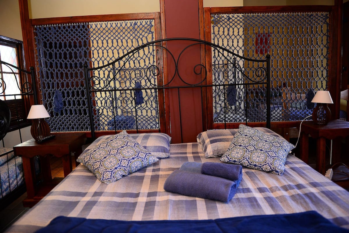 A neatly made bed with patterned pillows, a decorative metal headboard, and a view through a lattice window.