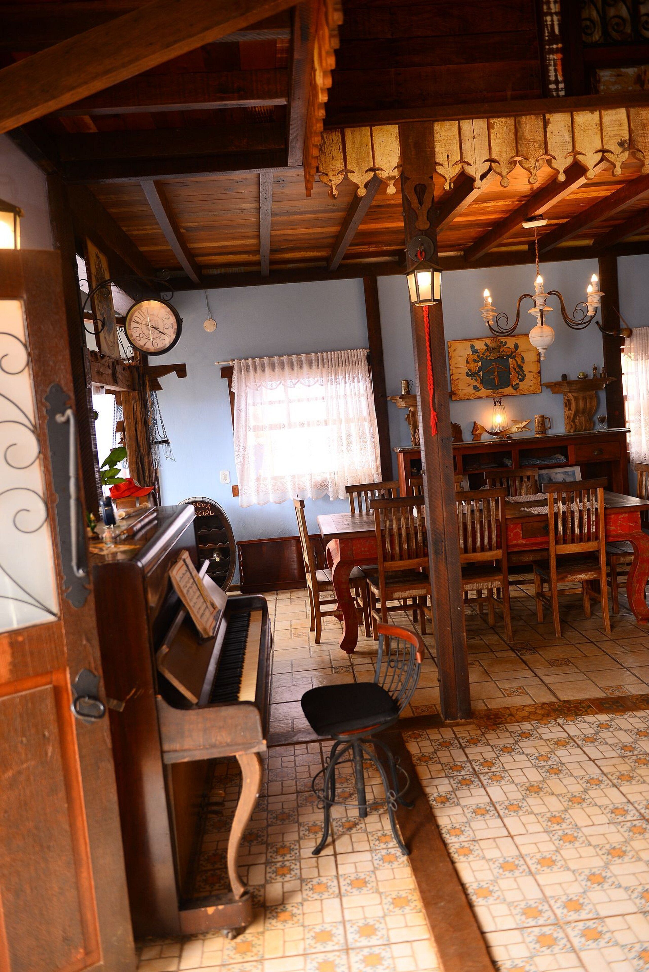 Una habitación acogedora con un piano, sillas de madera, una mesa de comedor y una araña.