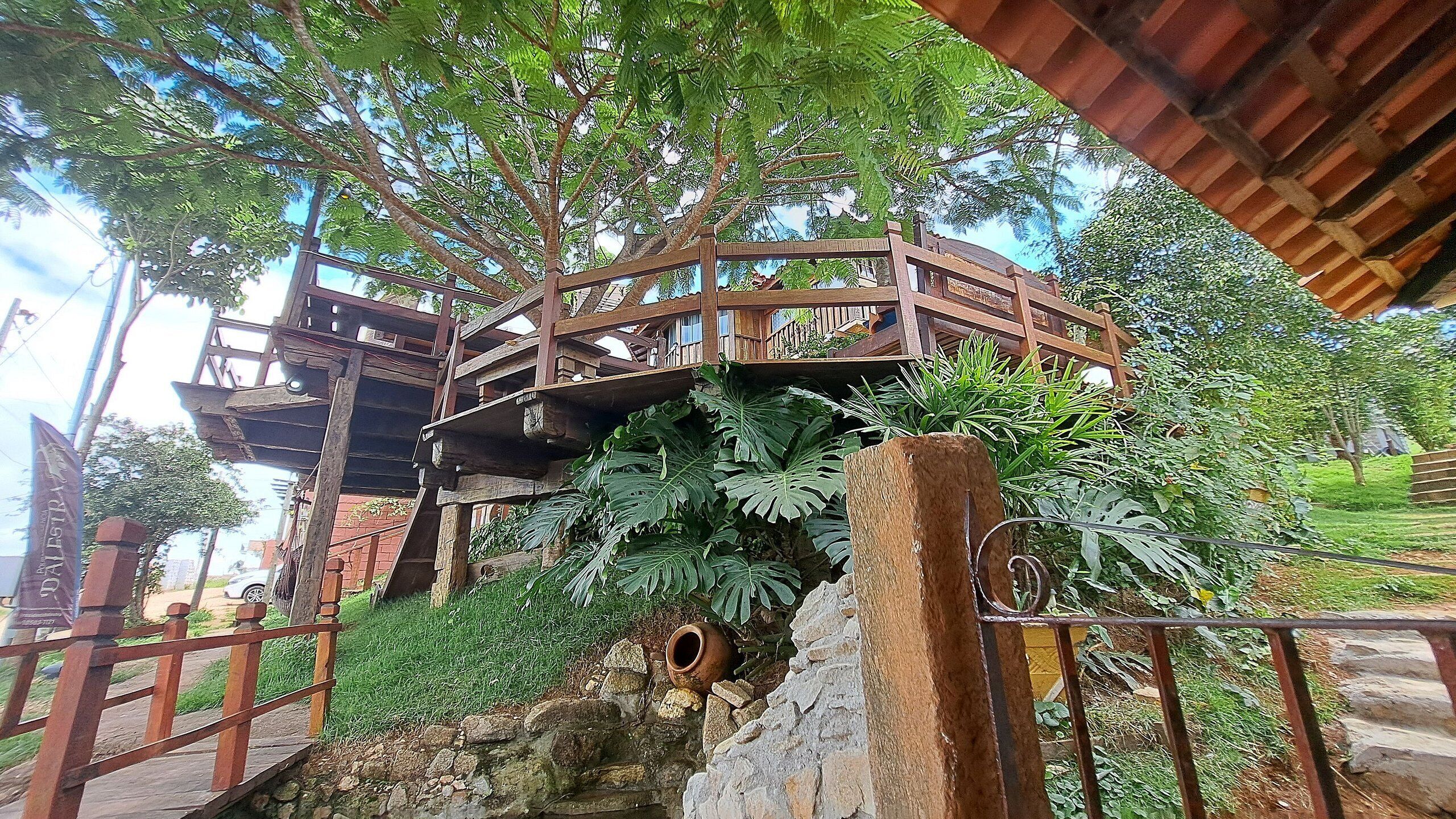 A wooden bridge connecting two elevated wooden structures amidst lush greenery.