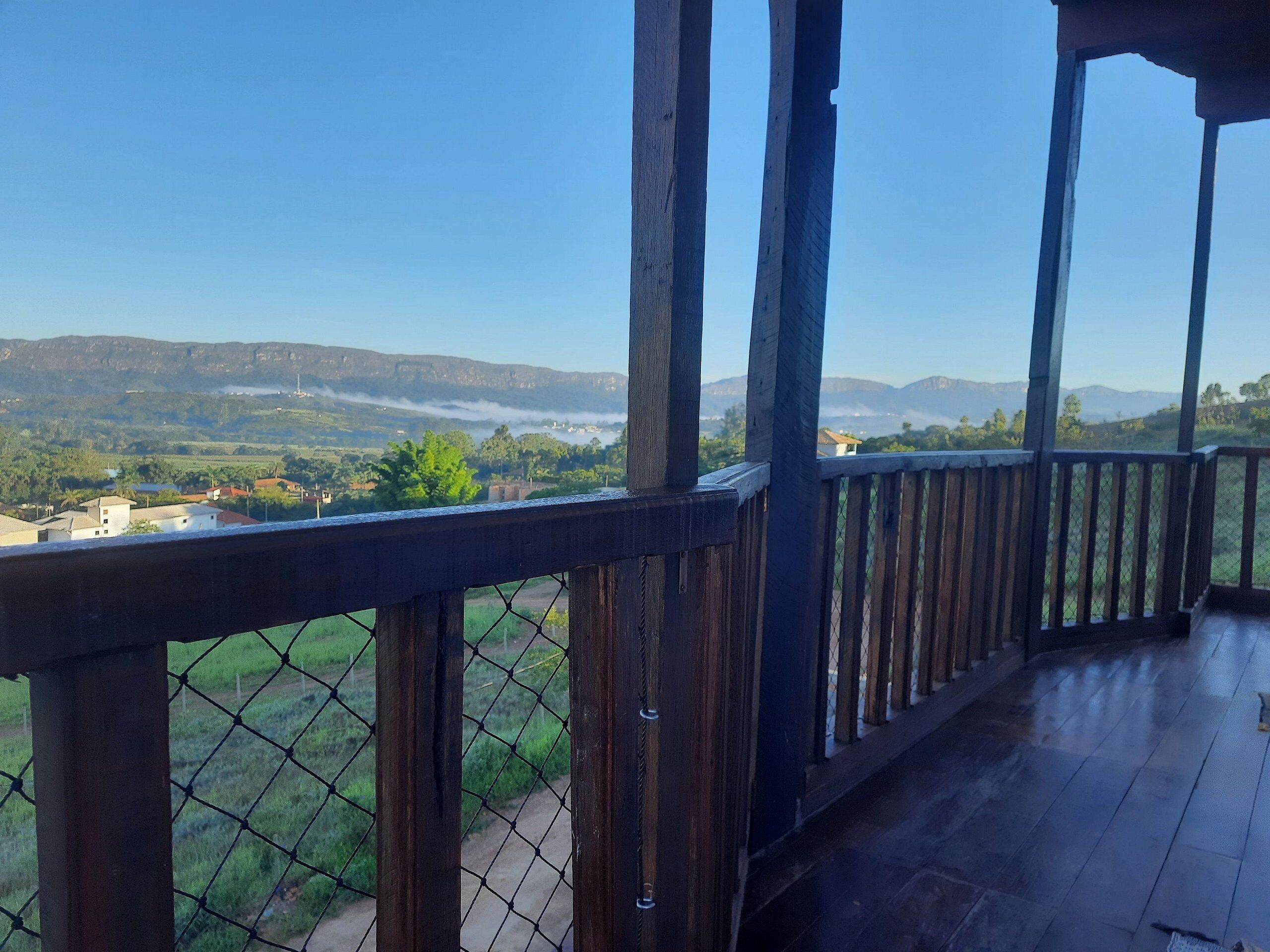 Un balcón de madera con una cerca de alambre que da a un paisaje montañoso bajo un cielo despejado.