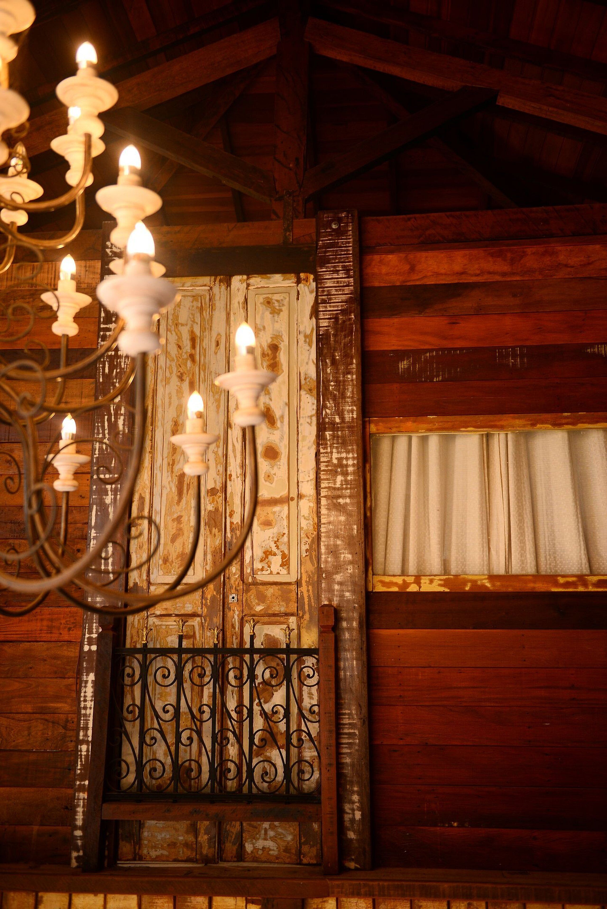 A rustic interior with a wooden wall, a window with curtains, and a wrought iron balcony railing.