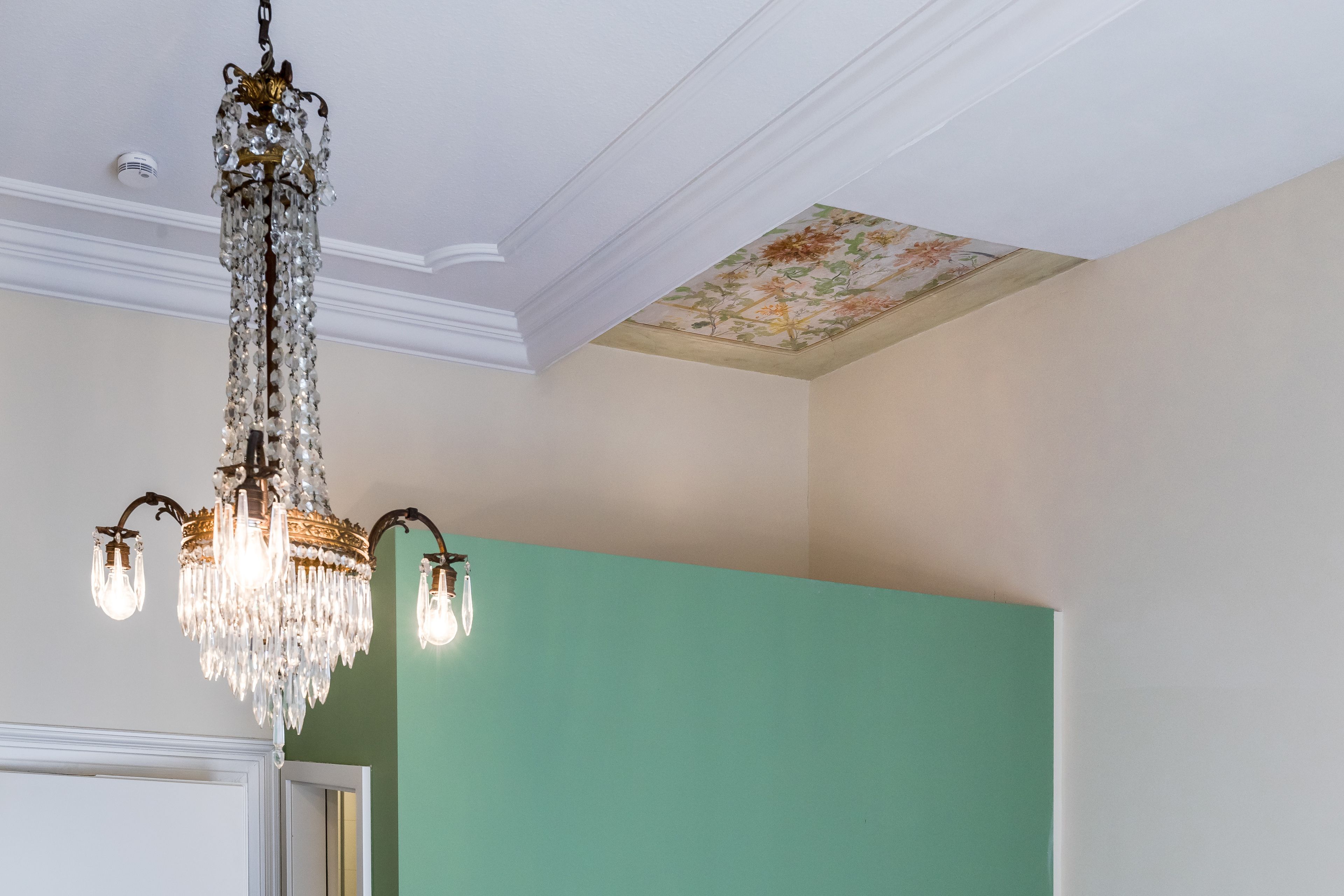 Une pièce dotée d’un lustre, d’un décor floral au plafond et d’un mur de couleur turquoise.