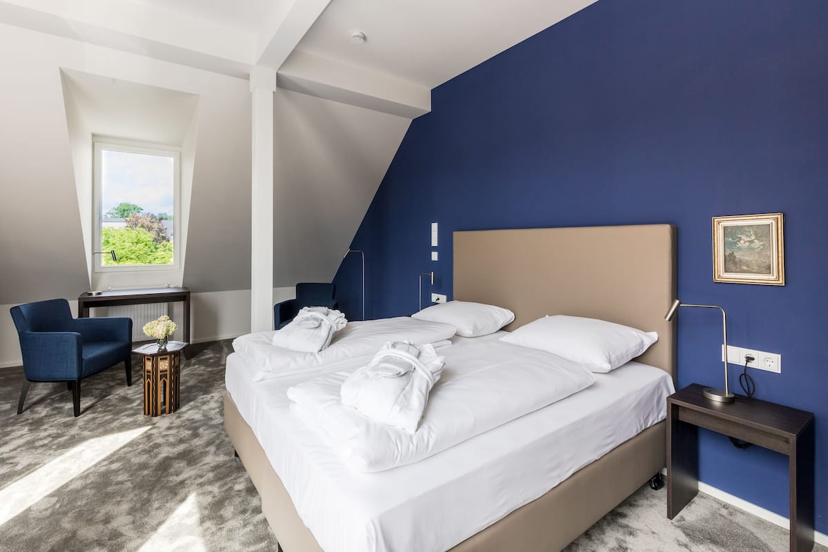 A hotel room with a large bed, a desk, a chair, and a view of greenery outside.